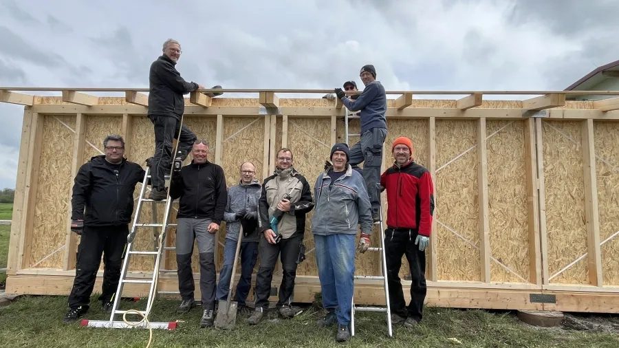 9 Männer stehen mit Werkzeug vor der Baustelle